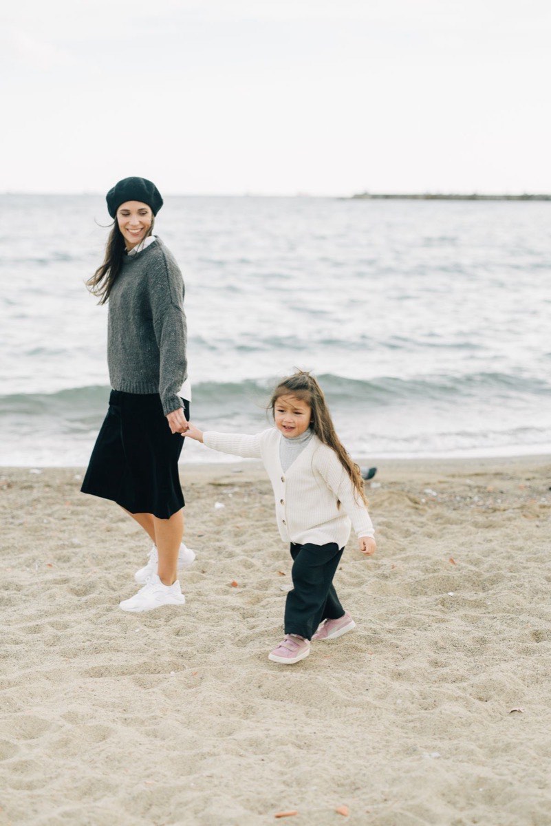 Madre e figlia sorridono camminando mano nella mano in riva al mare